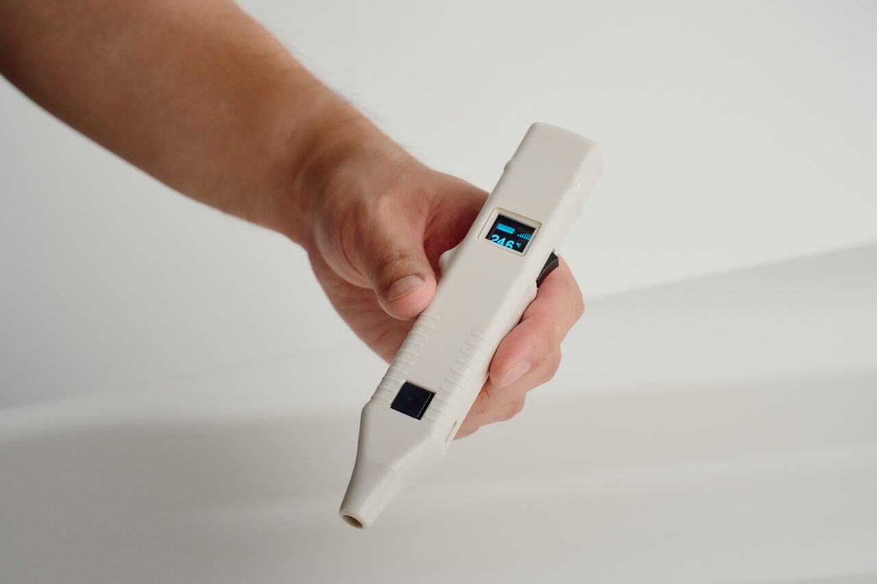 A hand holding the CRT LifeScan probe, its display showing a temperature reading
